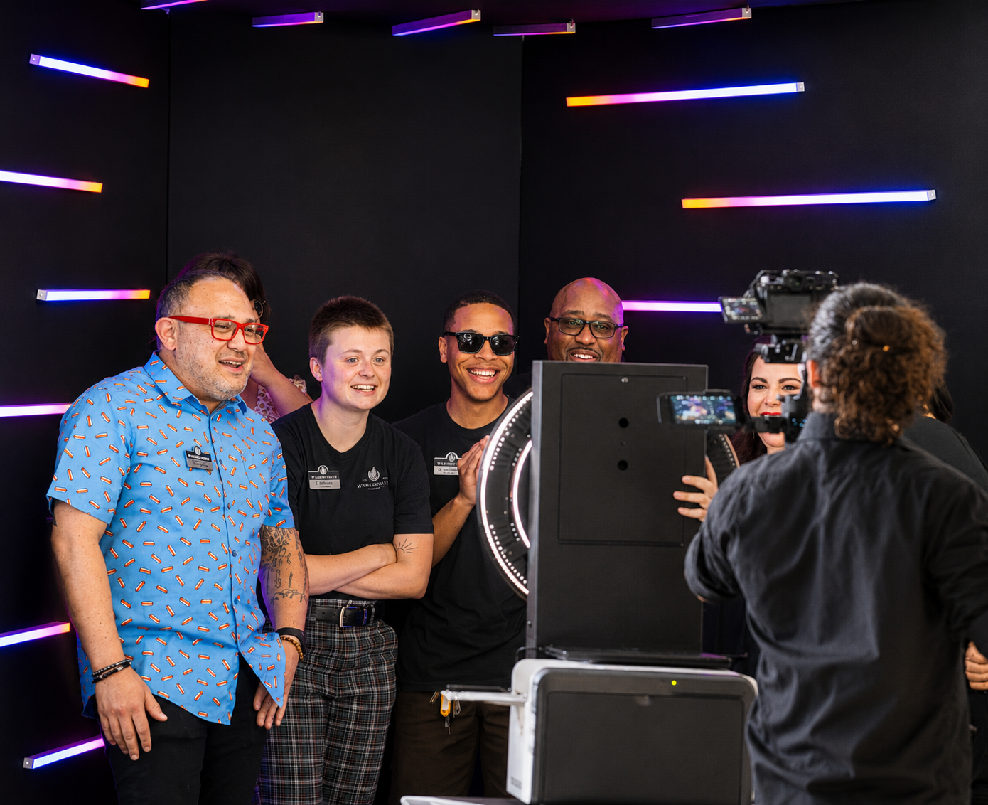 Group of smiling colleagues gathered around a photo booth at a corporate event with colorful neon lights