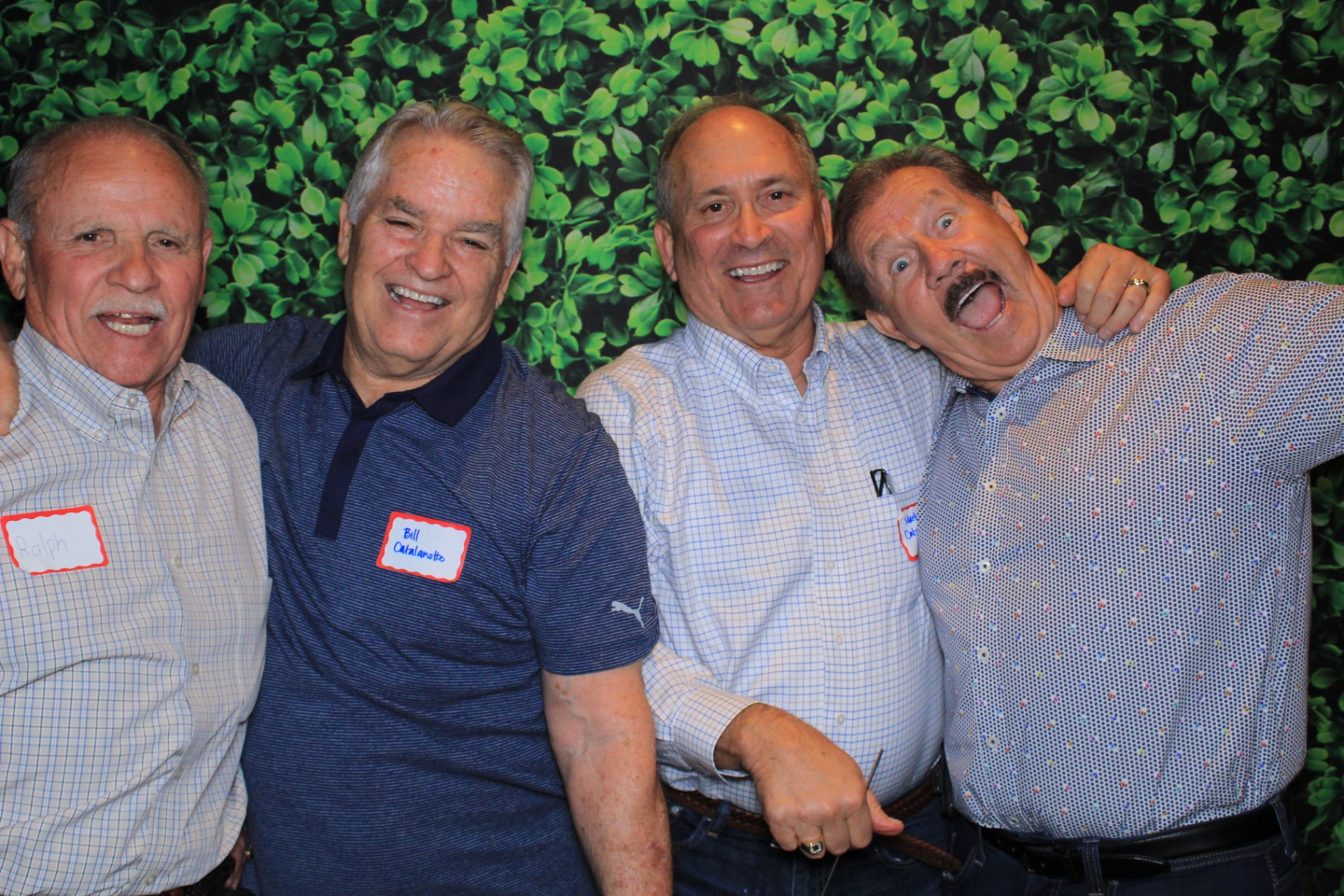 Group of friends laughing in front of a greenery wall