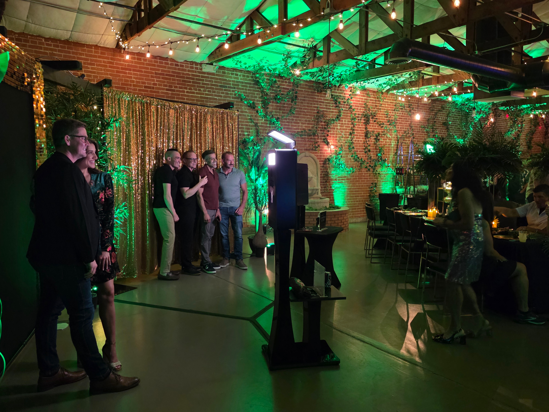 Guests posing at a gold sequin backdrop in a string-lit venue
