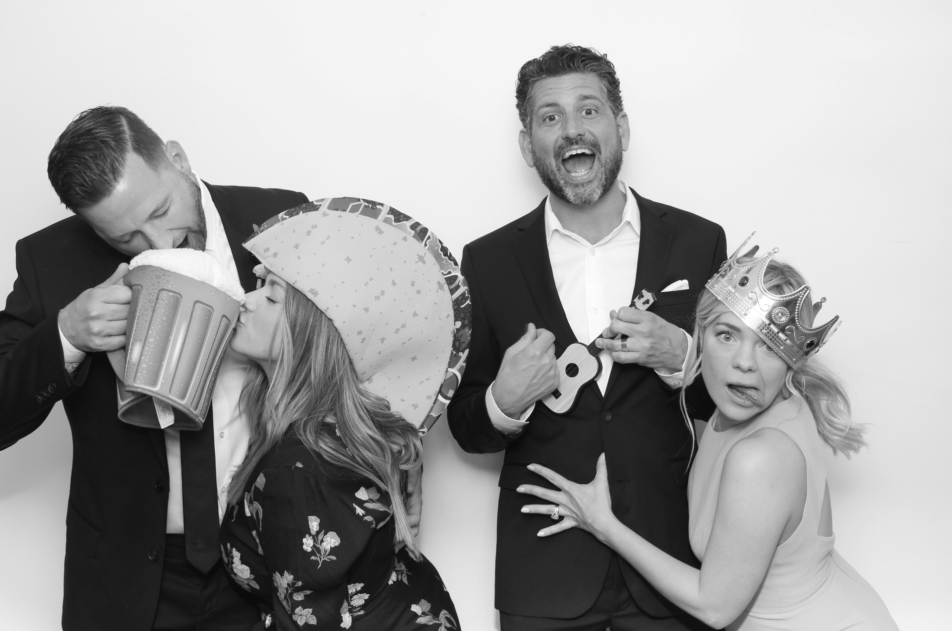 Wedding guests laughing with playful props in a black-and-white photo booth image